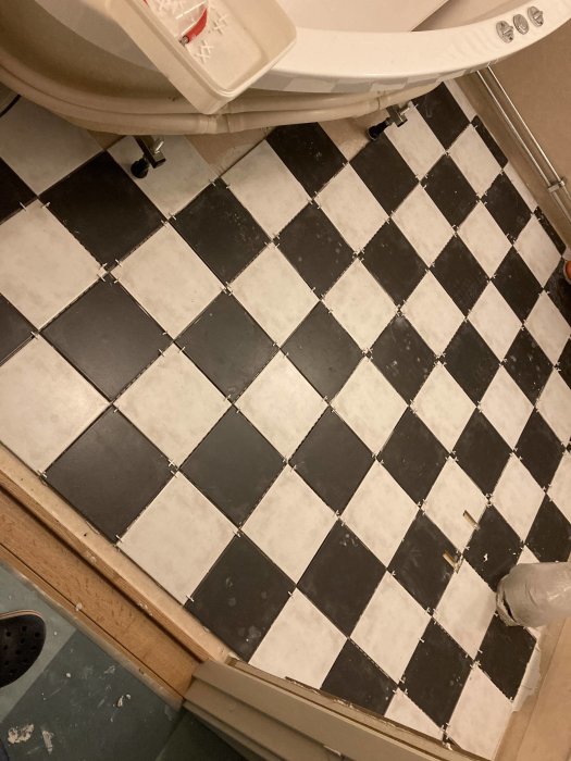 Nyinstallerat schackrutigt kakelgolv med fugor och kakelkors, nära en toalett, under renovering.