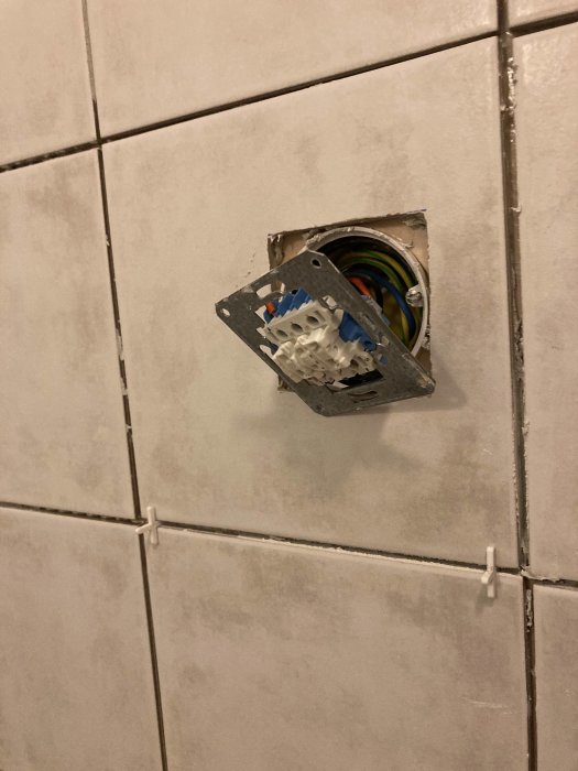 Eluttag utan väggplatta i en vägg med vita kakelplattor under installation eller reparation.
