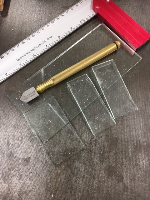 Glasskiva skuren i bitar med en metallskrapa och linjal på en arbetsbänk, används för orgelbygge.