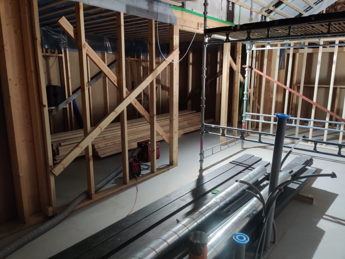 Byggarbetsplats med isolering, plastrullar och byggnadsmaterial vid en vägg under konstruktion.