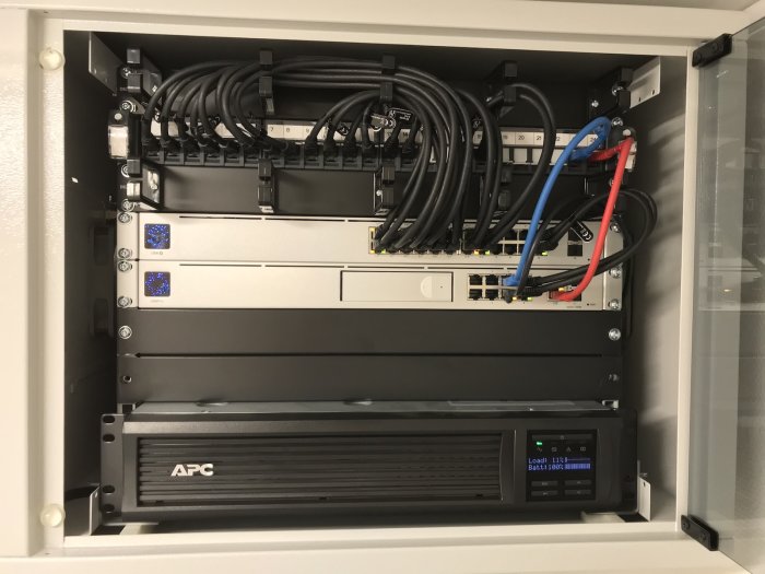 Nätverksskåp med UDM Pro, USW-24-POE switch och en APC Smart-UPS 750 UPS-enhet.