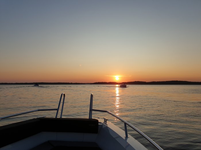 Vy från en båt med solnedgång över vattnet och andra båtar i fjärran.