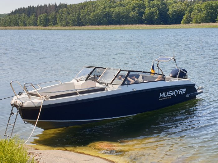 Motorbåt förtöjd vid kusten med skog i bakgrunden under en solig dag.