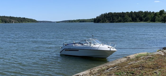 En vit 550 DC motorbåt förtöjd vid en strandkant nära skogklädda öar på en solig dag.