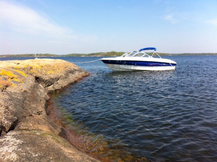 Motorbåt förtöjd nära klippor vid vattnet en solig dag.