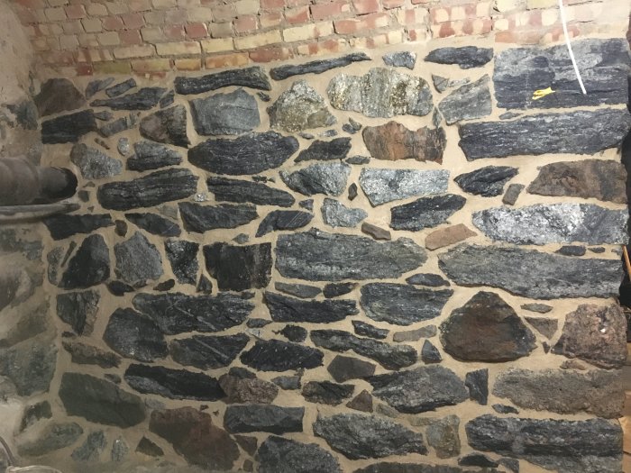 Nybyggd vägg med ett rustikt mönster av stora stenar och murbruk.