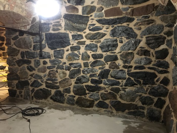 Nyrenoverade väggar med murat stenmönster i en inomhusmiljö med arbetslampa och kabel på golvet.