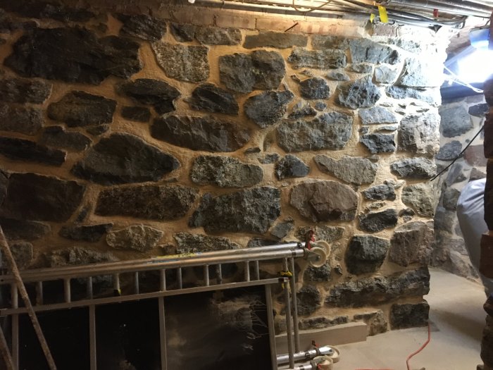 Nyrenoverad vägg med oregelbundna stenar och synlig fogmassa i byggmiljö.