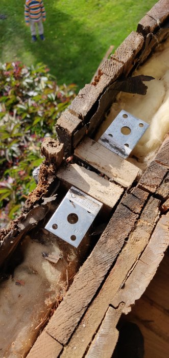 Närbild på äldre husväggs uppbyggnad med synliga isolerplattor, träreglar och metallbeslag, med suddig bakgrund.