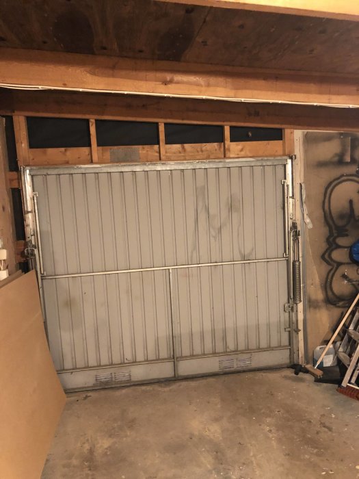Oisolerad garageport i ett kallgarage med synlig träram och ofullständig isolering ovanför.