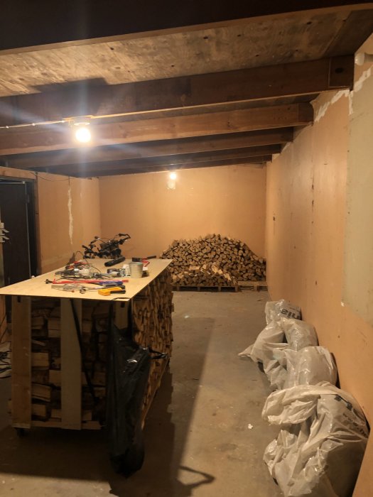 Interiör av kallgarage med oisolerade väggar och vedstapel, inklusive arbetsbänk med verktyg.