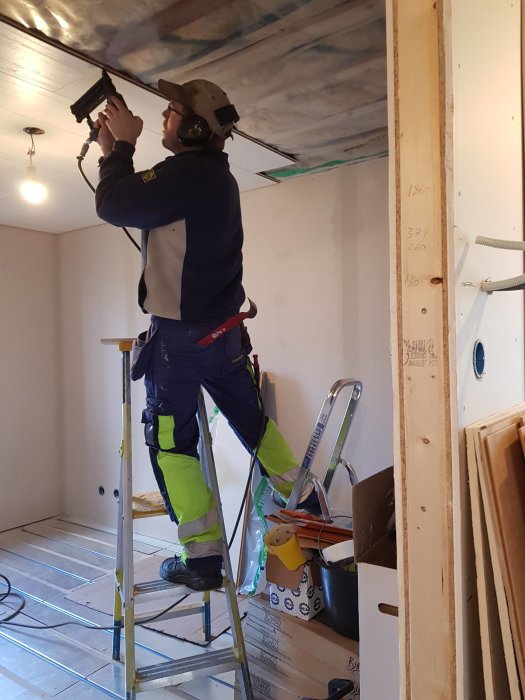 Arbetare installerar innertak medan han står på en stege i ett rum under renovering.