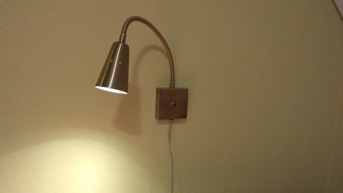 LED-vägglampa med flexibel arm, påslagen och monterad på en vägg ovanför strömbrytare.