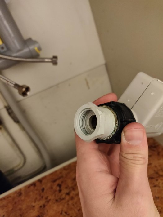 Hand håller en krananslutning för diskmaskin med ovanlig koppling i ett kök.