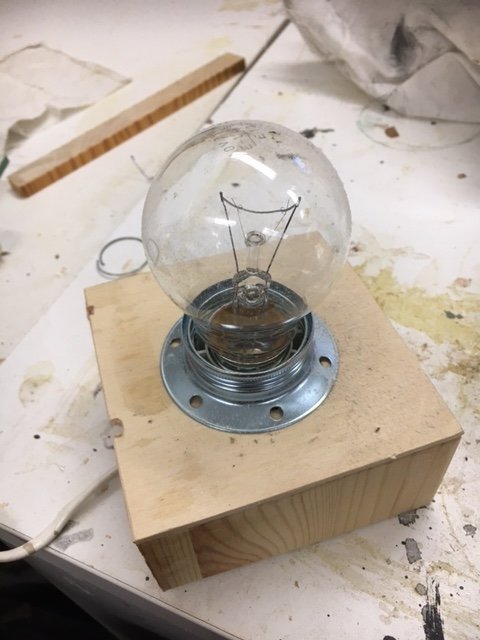 En glödlampa monterad i en metallsockel fastsatt på en träkub på en arbetsbänk.