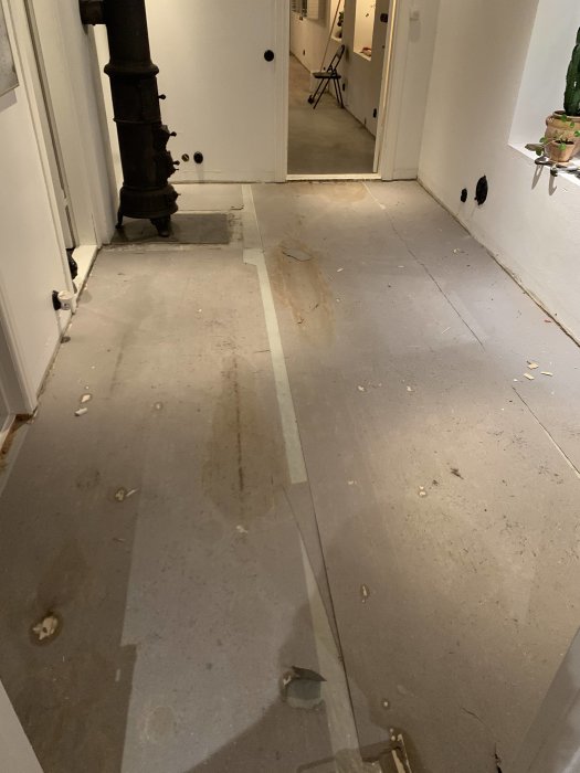 Skadat golv med fläckar och rester synliga efter att ha rivit bort övergolv i ett hus.