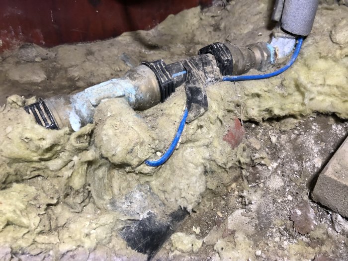 Ett rör med en blå värmekabel lindad omkring, omgiven av isolering, ser orörd ut i en oisolerad miljö.