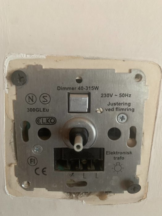 Söndrig dimmer med specifikationer "Dimmer 40-315W, 230V-50Hz" på vägg, märkt med "ELKO".