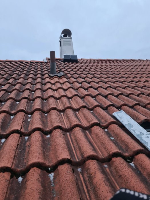 Ny takfläkt monterad på röd tegeltak mot grå himmel.