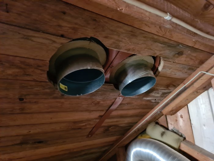 Två ventilationsrör installerade i ett träbjälklag på en vind.