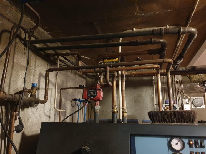 Kopparledningar och en cirkulationspump ovanför en värmepanna i ett pannrum.