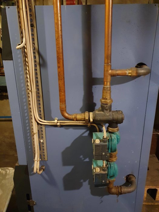 Värmesystem med kopparledningar och en Laddomat 3000 styrcentral mot en blå vägg.