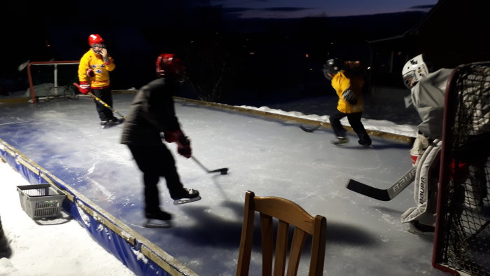 Kvarterslag spelar ishockey på bakgårdens hemmagjorda isrink under kvällsbelysning.