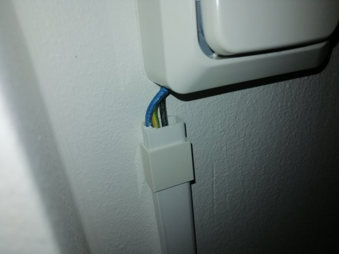Kabelkanal med synliga ledningar som ansluter till en strömbrytare, ser oavslutat och osäkert ut.