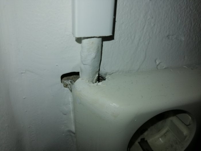 Oslagord kabelkanal till strömbrytare med synlig kabel och öppet hål ovanför vägguttag.