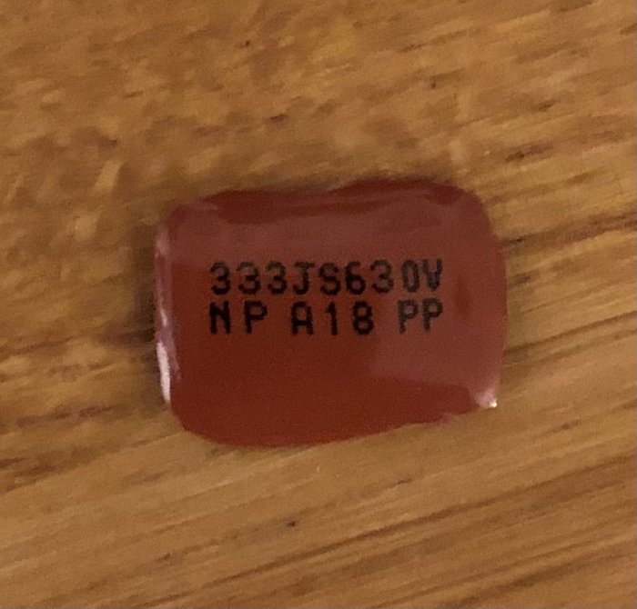 Bränd kondensator med texten "333J56N30V NP A18 PP" på en träyta.