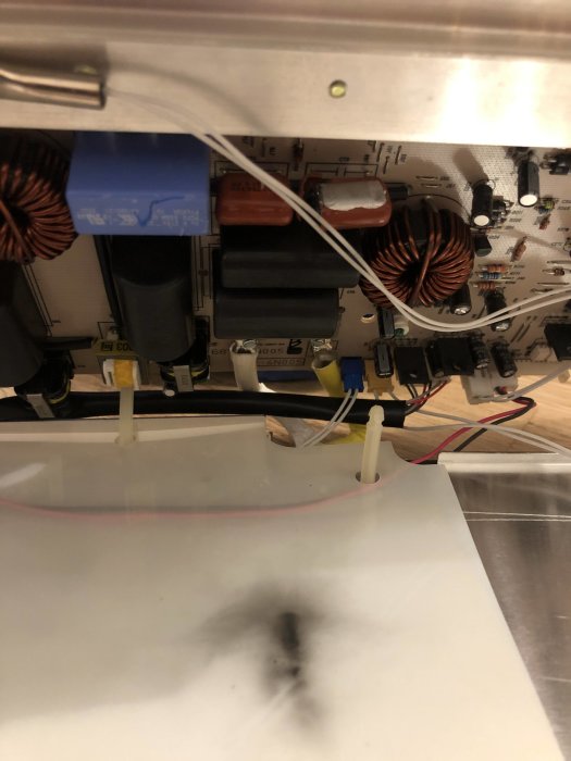 Interiör av en induktionshäll med en bränd kondensator och synliga elektriska komponenter.