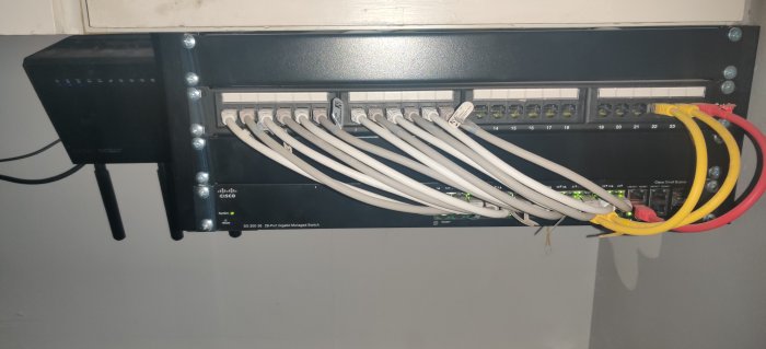 Cisco SG-300 switch och Asus router monterade i garage med ordnade nätverkskablar och en repeater.