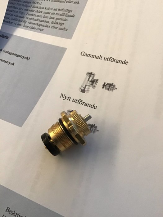 En termostatinsats för N-serien med 18mm gänga bredvid instruktionspapper som jämför gammalt och nytt utförande.