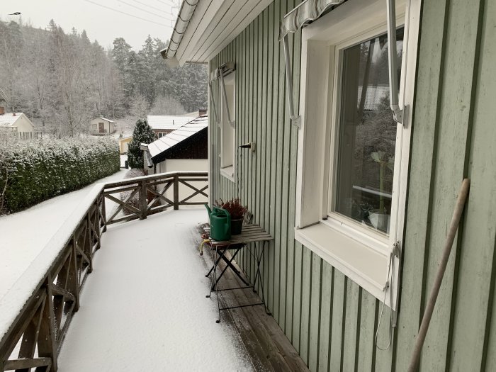 Snötäckt veranda på ett grönt Älvsbyhus med inåtgående fönster i söderläge under en snöig dag.