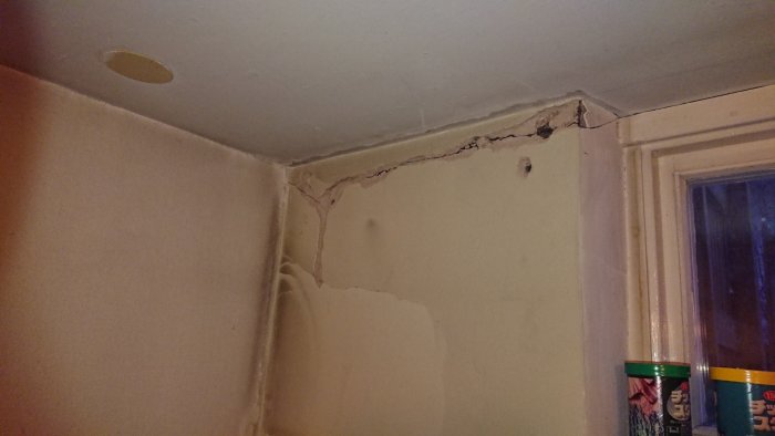 Sprickor i hörnet av en källarvägg vid taket, intill ett fönster, efter borttagen panel.