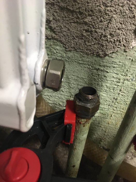 Närbild av en radiator ansluten till rörledningar med läckage vid returventilen.