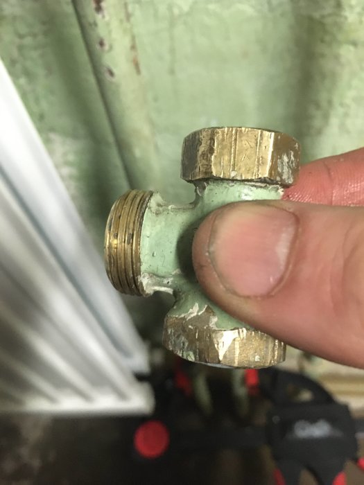Närbild på en hand som håller en radiatorventil med synligt läckage och gammal packning.