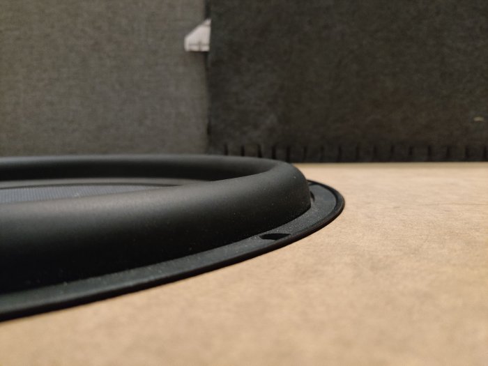 Närbild på baslådans svarta högtalarelement under provmontering mot brun bakgrund.