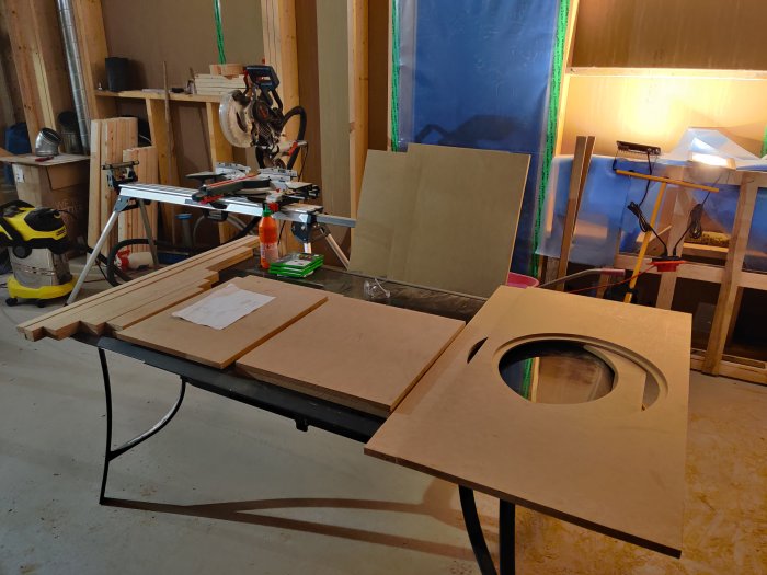 Trähantverksprojekt med utskuret element till baslåda på en arbetsbänk i ett pågående byggområde.