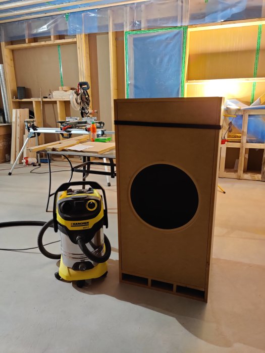 En nybyggd, obehandlad baslåda till hemmabio vid en arbetsbänk och kap-/gersåg i ett under konstruktion.