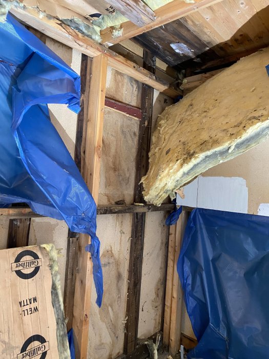 Vägg med fuktskador och dålig isolering; synliga reglar, pressening och mineralull.