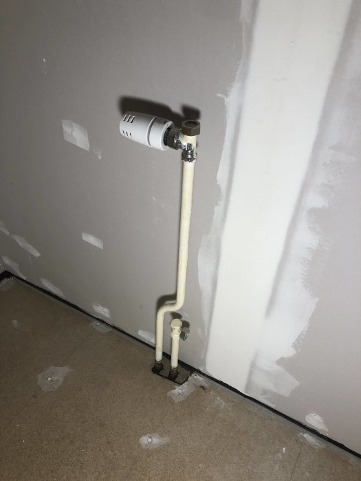 Gamla järnrör för radiator framför en gipsvägg som förbereds för renovering.