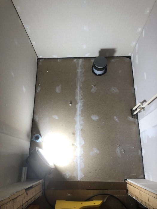 Ett hörn av en ofärdig toalettrenovering med synliga rör i väggen och golv under arbete.