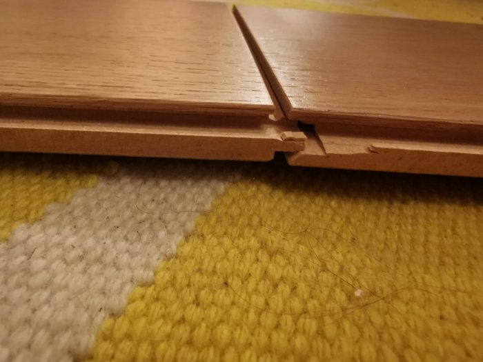 Närbild på ej ihopsatt ekparkettgolv med synlig klickfog över gul och vit matta.