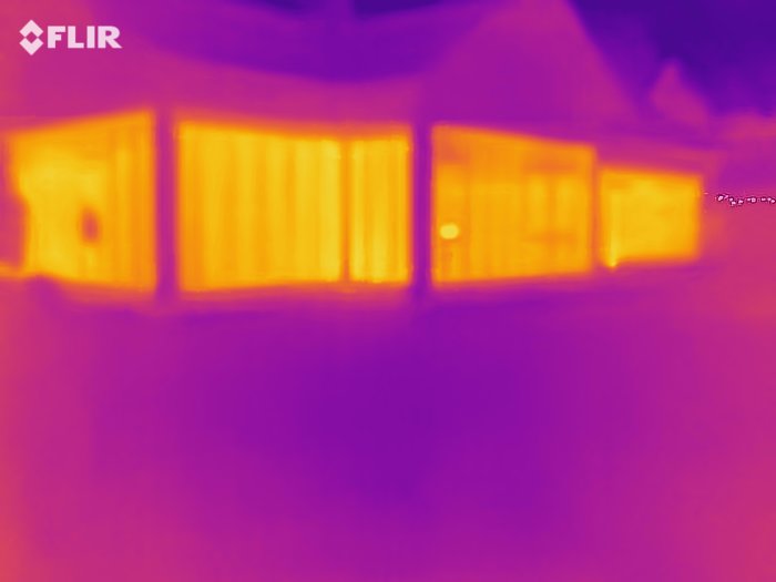 Termografisk bild av ett hus som visar värmeutstrålning genom fönster och väggar.