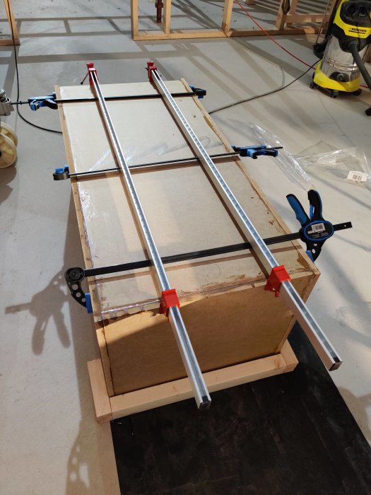 Trähögtalarlåda under konstruktion med skruvtvingar och limknektar i en verkstad.