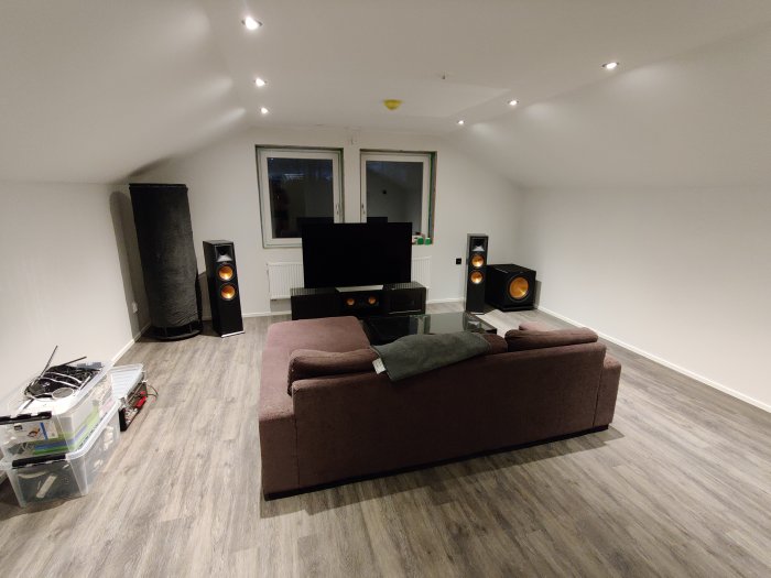 Vardagsrum med hemmabyggd Sonosub, Klipsch högtalare, soffa och TV, med byggmaterial på golvet.