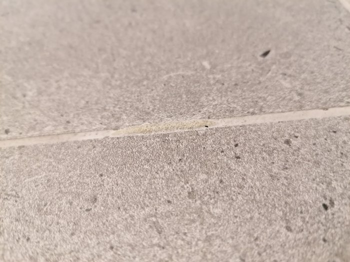 Förhöjningar i fog mellan grå kakelplattor, ser ut som hårdnad massa.