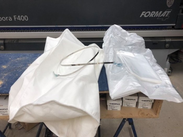 Ny vit filtersäck och armerad spånsäck för spånsug ligger på ett arbetsbord i en verkstad.