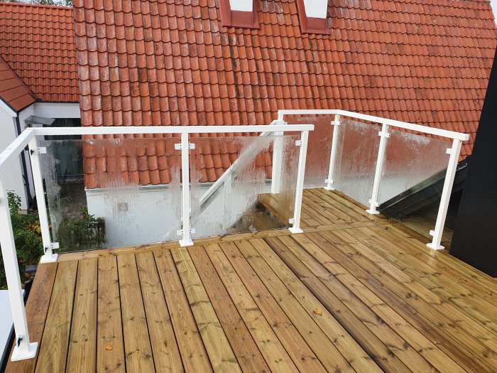 Träterrass med nyinstallerat vitt räcke, bredvid röda tegeltak och vita husväggar.